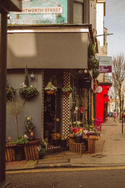 A storefront displaying a variety of fresh flower arrangements and potted plants outside a flower shop on Harlesden High Street. The floral display includes colorful bouquets with pink, yellow, and pu