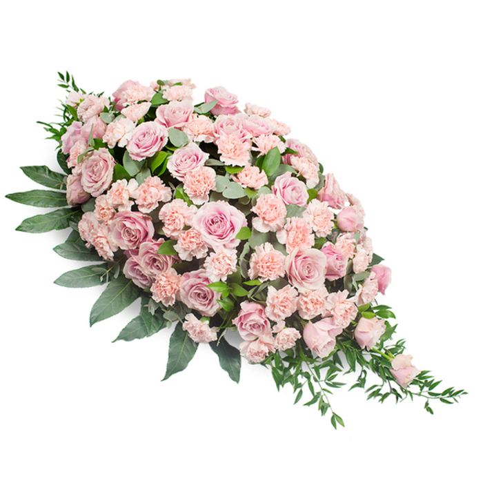 A refined funeral spray in a classic teardrop silhouette is displayed on a bright white background, its form starting broad and full at the top left and then tapering gracefully to a fine point at the lower right. The surface of the arrangement is densely packed with pastel blooms, primarily soft pink roses combined with light peach-pink carnations, giving the spray a romantic, tranquil presence. Many of the roses are fully open, revealing layered, velvety petals that curl gently at the edges, while a few slightly tighter heads add depth and variation. Their colours range from delicate blush to a more muted, vintage pink, reminiscent of the gentle tones often chosen by families in Harlesden for a dignified farewell. Nestled between the roses, clusters of ruffled carnations in pale peach-pink fill the spaces with feathery texture, their frills softening every transition from one bloom to the next. This interplay of shapes and shades makes the spray appear continuous and complete, with no harsh lines or gaps. Supporting the flowers is an abundance of dark green foliage: broad, smooth leaves create a structured base along the outer edges, while slimmer stems and finer sprigs of greenery weave among the blossoms and extend slightly beyond the tip, suggesting quiet, natural movement. Against the crisp white background, the pastel flowers and foliage stand out clearly, allowing every petal and leaf to be distinguished. The overall mood is serene, respectful, and comforting, ideal for placement on a casket, at the front of a chapel in Harlesden, or beside a framed photograph at a memorial gathering near Roundwood Park. Crafted with the care of a local florist who understands the importance of saying goodbye beautifully, this spray embodies love, remembrance, and a gentle sense of peace.