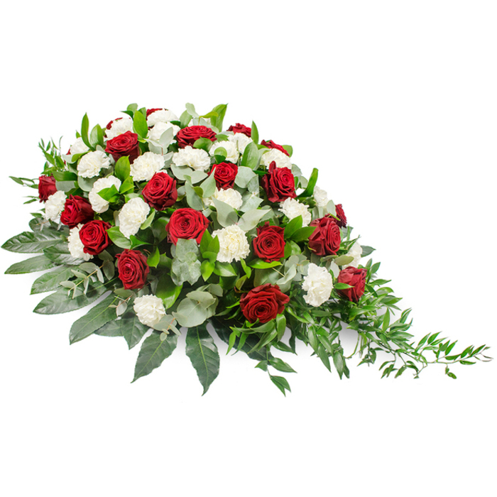 This image shows an elegant funeral flower spray laid on a plain white background, its details clearly defined as though waiting to be carefully carried into a chapel in Harlesden. The overall shape is elongated and horizontal, fuller and more layered on the left, then gently diminishing to a soft, trailing point on the right, creating the impression of a subtle, one-directional flow. The heart of the arrangement is a classic combination of deep red roses and white carnations. The roses, with their rich, velvety petals still wrapped closely around their centers, are scattered throughout the design, each bloom conveying profound love, honour, and the sorrow of saying farewell. Interspersed between them are numerous white carnations, their petals densely ruffled and slightly tufted, bringing a softer, cloud-like texture and a sense of purity and blessing. The flowers are supported by an abundant base of green foliage. Broad, dark green leaves form a strong, glossy foundation, while paler, silvery-green eucalyptus leaves are woven among the blooms, adding depth, contrast, and an understated, herbal fragrance. From the right-hand side, finer stems of lighter green foliage trail gracefully outward, lending the tribute a natural, almost river-like line, as if gently guiding the gaze towards the front of a service. The lighting is even and calm, casting soft shadows that emphasise the mound of flowers without harshness. The red, white, and green palette feels solemn and timeless, typical of memorial flowers chosen for funerals, wakes, or graveside tributes around Harlesden's local churches and cemeteries. The arrangement suggests a piece designed to rest flat, perhaps on a casket or as a central feature at a remembrance gathering, offering a dignified, floral expression of sympathy and enduring memory.